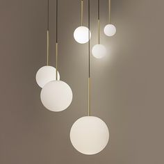 five white and gold colored lights hanging from the ceiling in front of a gray wall