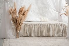 there is a bed with white sheets and drapes on the headboard, next to some dried grass