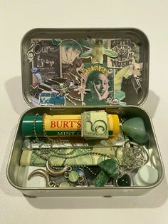 an open tin with various items in it on a white surface, including money and other things