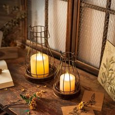 two lit candles sitting on top of a wooden table next to pictures and papers with flowers