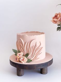 a pink cake sitting on top of a wooden stand next to a vase with flowers