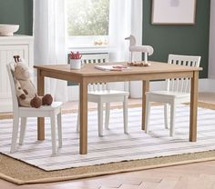 a child's wooden table and chairs in a room with green walls, rugs and white curtains