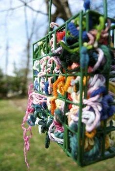 a green basket filled with lots of colorful crocheted items hanging from it's sides