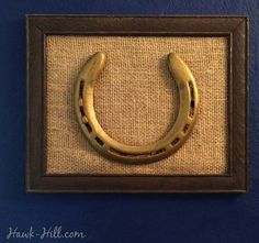 a gold horseshoe hangs on a blue wall with burlap and wood framed artwork