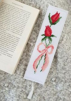 a cross stitch bookmark with a red rose on it next to an open book