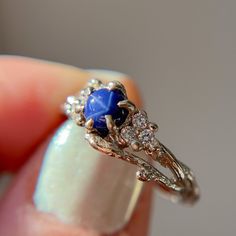 a woman's hand holding a ring with blue stone and diamonds on it,