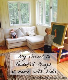 a little boy writing on a blackboard in front of a living room with white furniture