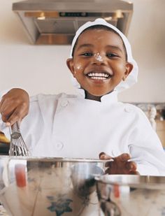 a young boy in chef's outfit mixing food in a bowl with a whisk