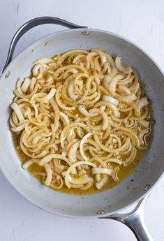 a skillet filled with noodles and sauce on top of a white countertop next to utensils