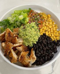 a white bowl filled with black beans, corn and guacamole next to lettuce