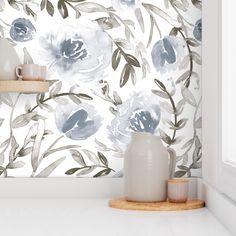 a white vase sitting on top of a counter next to a wallpaper covered in blue flowers