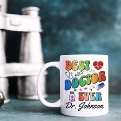 a white coffee mug with the words best doctor ever on it next to a pair of scissors