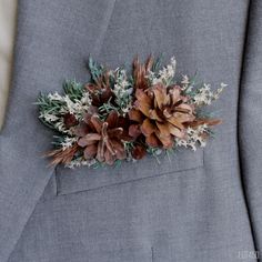 a boutonniere with pine cones and white flowers on the lapel of a man in a gray suit