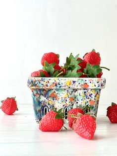 some strawberries are in a flower pot on the table next to other strawberries