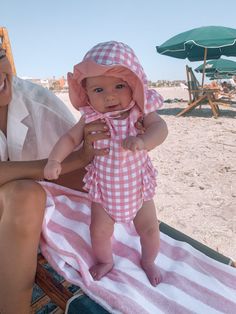 a woman sitting on top of a towel next to a small baby in a pink and white checkered dress