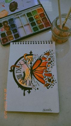 an open notebook with a butterfly drawn on it next to a paintbrush and watercolor palette