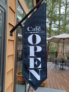 an open sign hanging from the side of a building next to a patio with tables and umbrellas