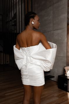 the back of a woman in a white dress with her hands on her hips, looking off to the side