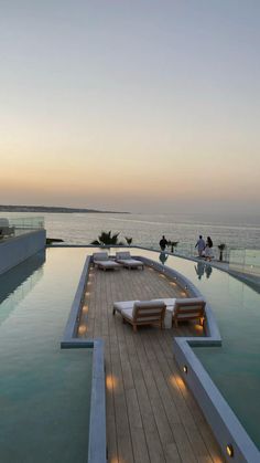 an outdoor swimming pool with lounge chairs and lights on the deck next to the water