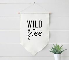 a white wall hanging with the words wild and free on it next to a potted plant