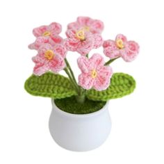 small crocheted pink flowers in a white vase with green leaves on the bottom