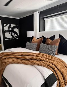 a bedroom with black walls and white bedding, brown throw pillows and blankets on the headboard