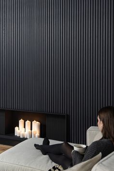 a woman sitting on a couch in front of a fireplace with lit candles behind her