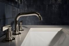 a white sink sitting under a faucet next to a wall mounted soap dispenser