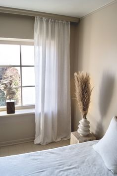 a white bed sitting next to a window in a bedroom under a large pair of curtains