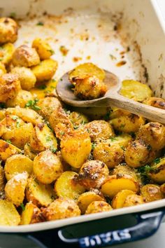 a pan filled with cooked potatoes and parsley on top of a table next to a wooden spoon