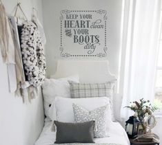 a white bed sitting under a window next to a wall with a quote on it