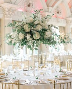 an elegant wedding reception with white flowers and greenery in tall gold centerpieces