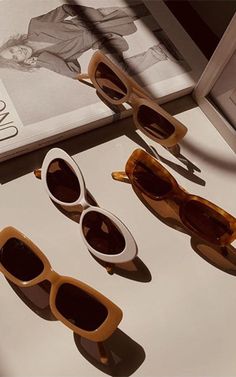 three pairs of sunglasses sitting on top of a table next to an open book and magazine