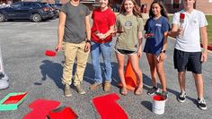 four young people standing in front of a building with numbers painted on the ground and buckets