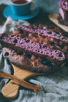 a loaf of bread with blueberries on it sitting on a cutting board next to a cup of tea