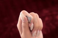 a woman's hand holding a diamond ring on top of her finger, in front of a red velvet background