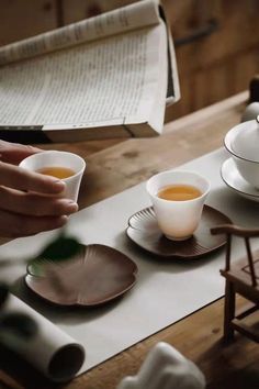 two cups of tea sit on a table next to an open book and folded napkins