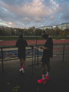 two people standing next to each other in front of a tennis court with the sky behind them