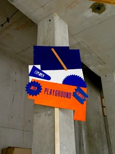 an orange and blue sign hanging from the side of a cement pillar in a building