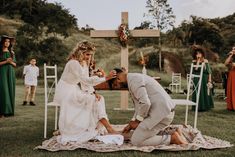 a man kneeling down next to a woman on top of a blanket in front of a cross