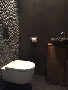 a white toilet sitting in a bathroom next to a sink and wall mounted faucet