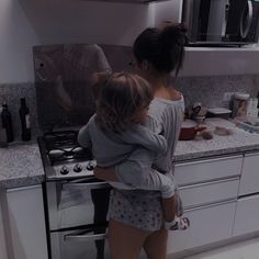 a woman holding a child in her arms while standing in front of a stove top oven