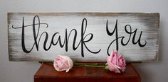 two pink roses sit on top of a wooden sign that says thank you with black lettering