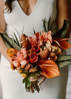 a woman in a white dress holding a bouquet of orange and pink flowers on her wedding day