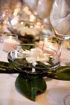 candles and flowers are on the table with wine glasses, napkins and glassware