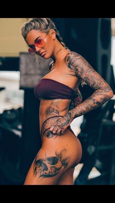 a woman with tattoos on her body standing in front of a car and looking at the camera