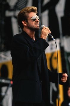 a man with sunglasses on holding a microphone in front of him and singing into the microphone