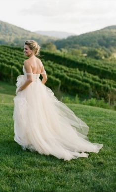 a woman in a wedding dress is standing on the grass looking off into the distance