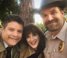 two men and a woman posing for a photo in front of a tree with a police officer standing next to them