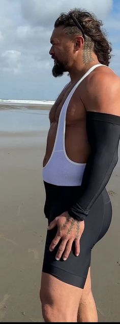 a man with long hair and tattoos on his arm standing in the sand at the beach